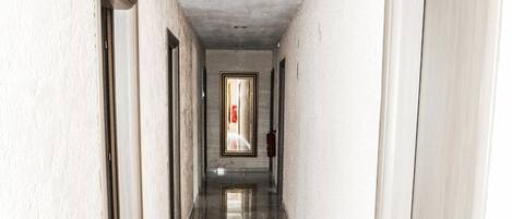 Un pasillo con paredes blancas y suelo de mármol, que conduce a una puerta al final.