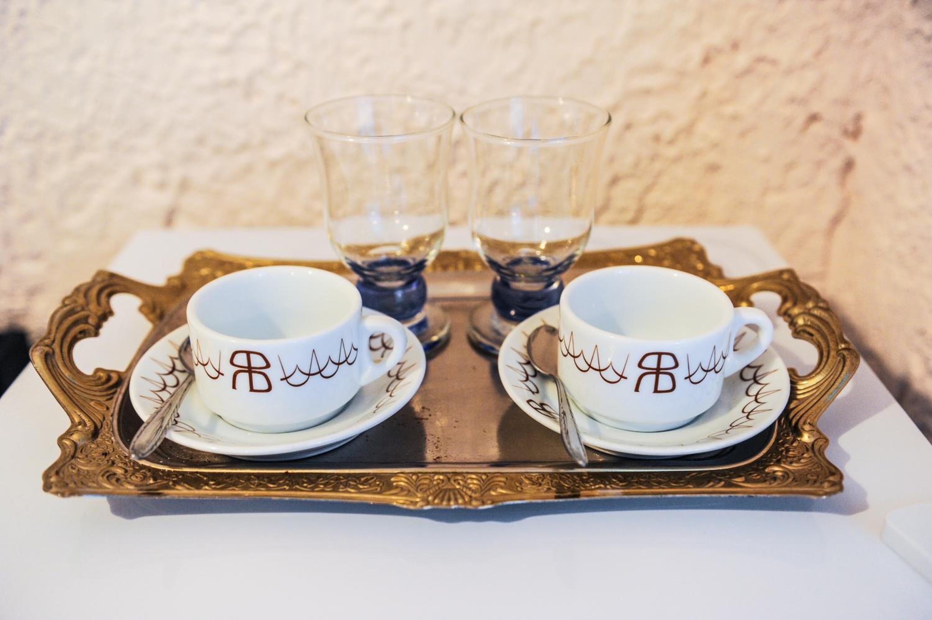 Dos tazas blancas con diseños marrones sobre una bandeja dorada.