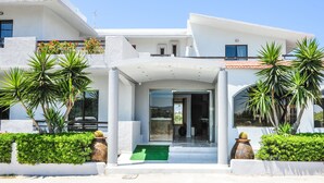A modern white building with a covered entrance, glass doors, and a green mat. - Valentino Hotel (Rhodes)