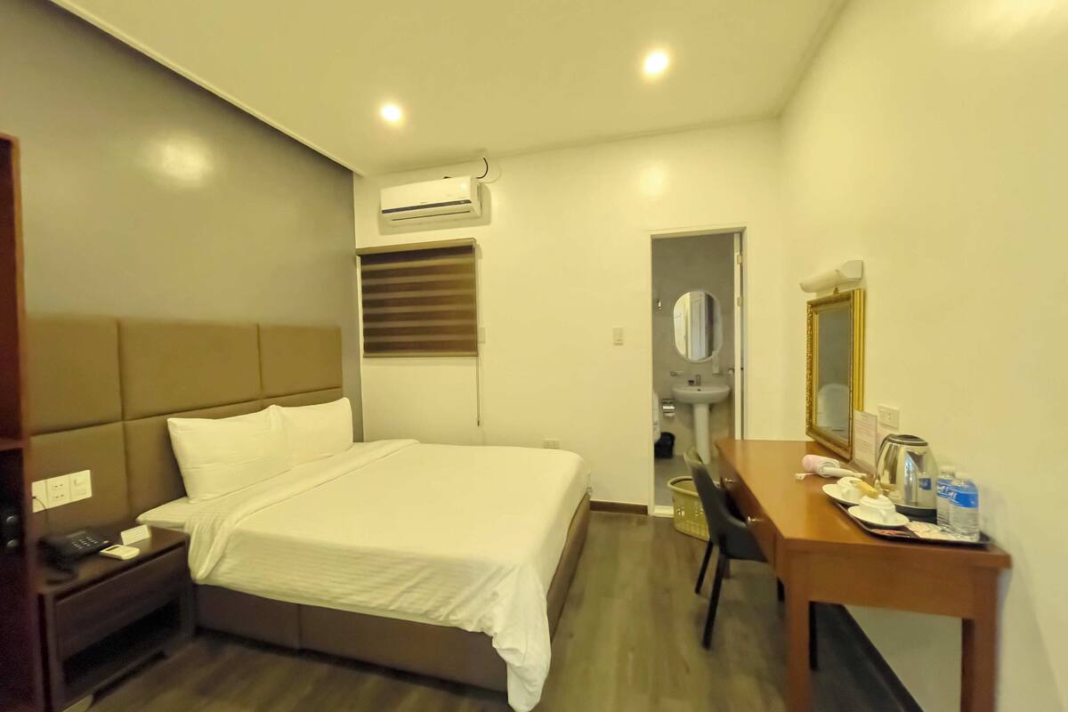 Een hotelkamer met een bed, nachtkastje, bureau, stoel en een spiegel.