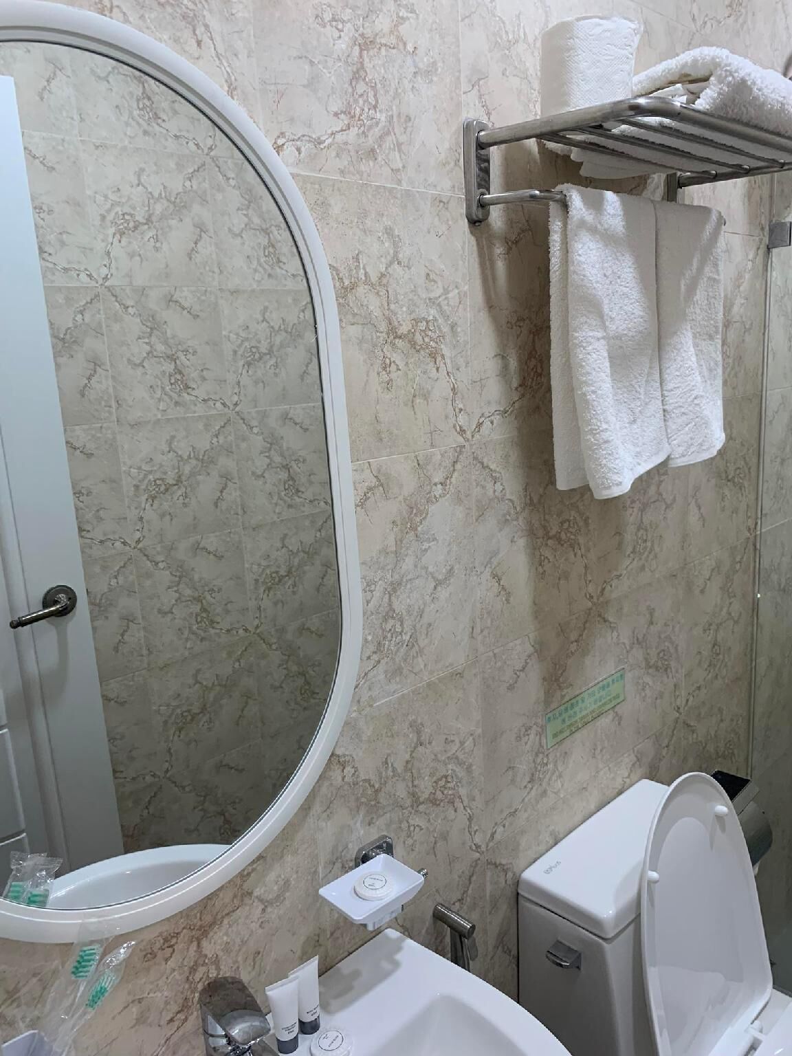 A bathroom with a marble wall, a toilet, a sink with a mirror, and a towel rack with a white towel.