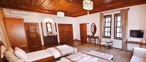 A hotel room with wooden ceilings, two beds with white linens, a small table, a chair, a television, and a window with curtains.