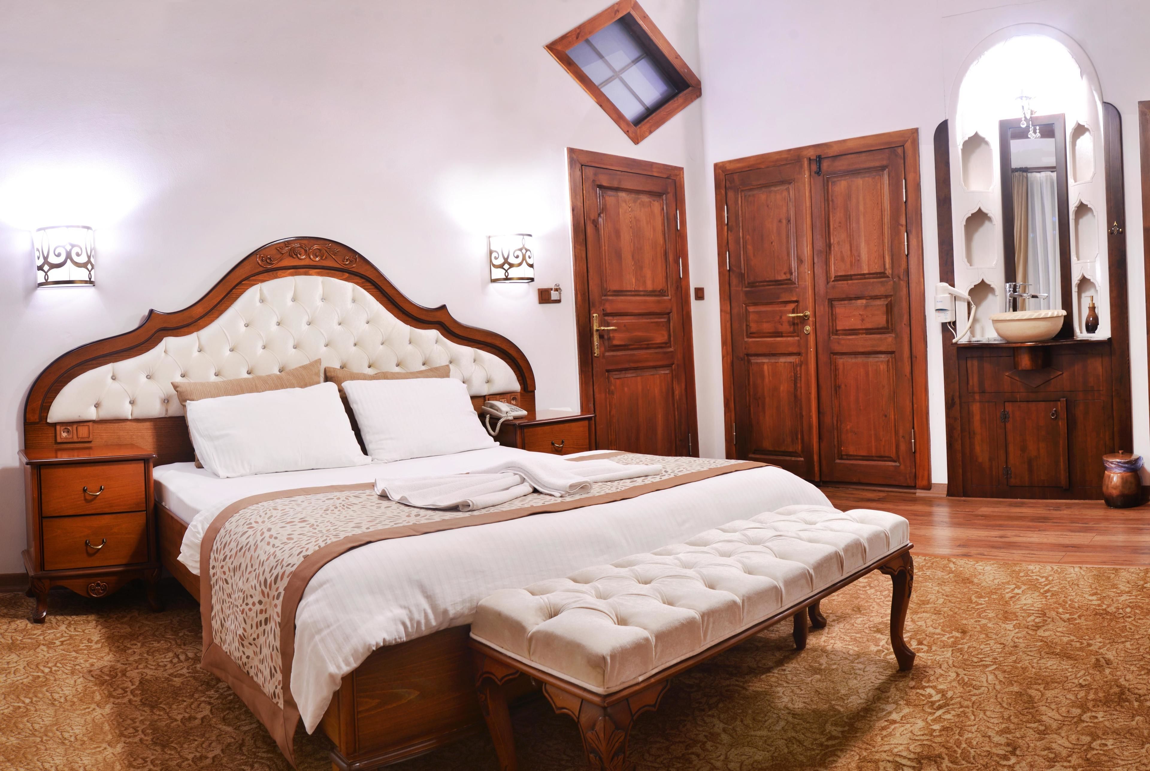 A bedroom with a large bed, wooden wardrobe, and a small bathroom with a mirror and sink.