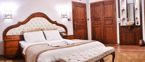 A bedroom with a large bed, wooden wardrobe, and a small bathroom with a mirror and sink.