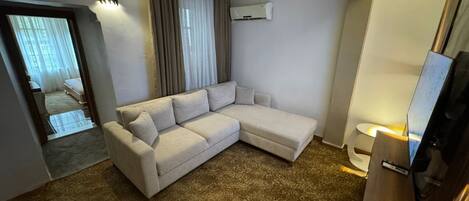 Habitación de hotel moderna con sofá modular, televisión de pantalla plana, equipo de aire acondicionado y alfombra estampada.