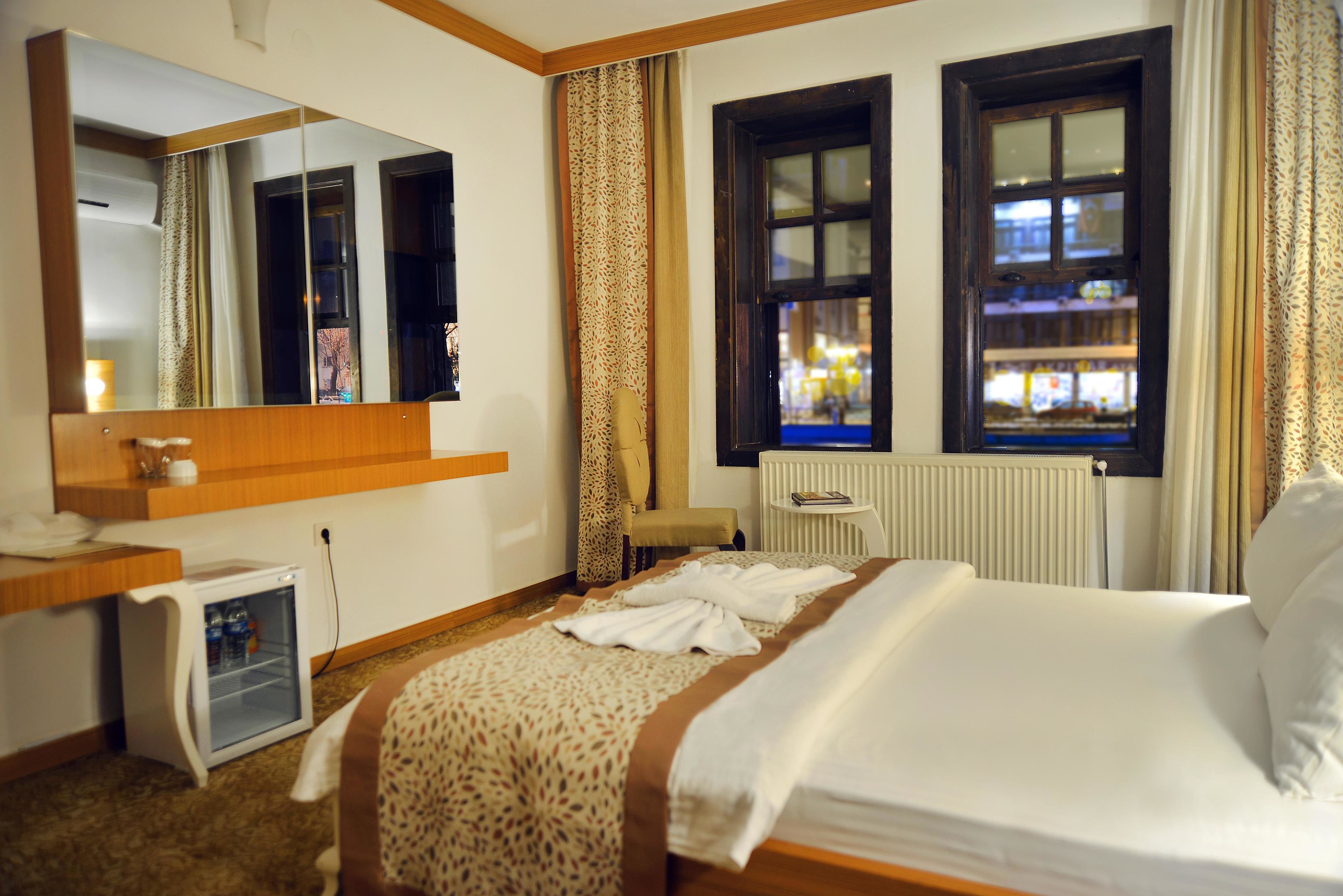 Une chambre d’hôtel comprenant un lit, un petit bureau avec un réfrigérateur, un miroir, une fenêtre avec des rideaux et un radiateur.