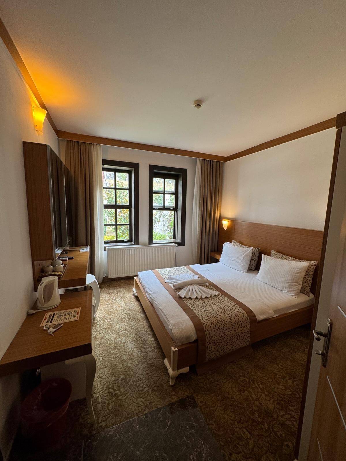 Une chambre d’hôtel avec un lit, une table de chevet, une lampe et une fenêtre avec des rideaux.
