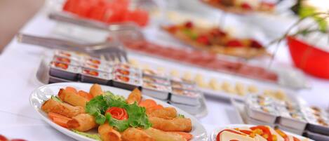 Una mesa de buffet con diversos alimentos, entre ellos aperitivos fritos, ensaladas y fruta.