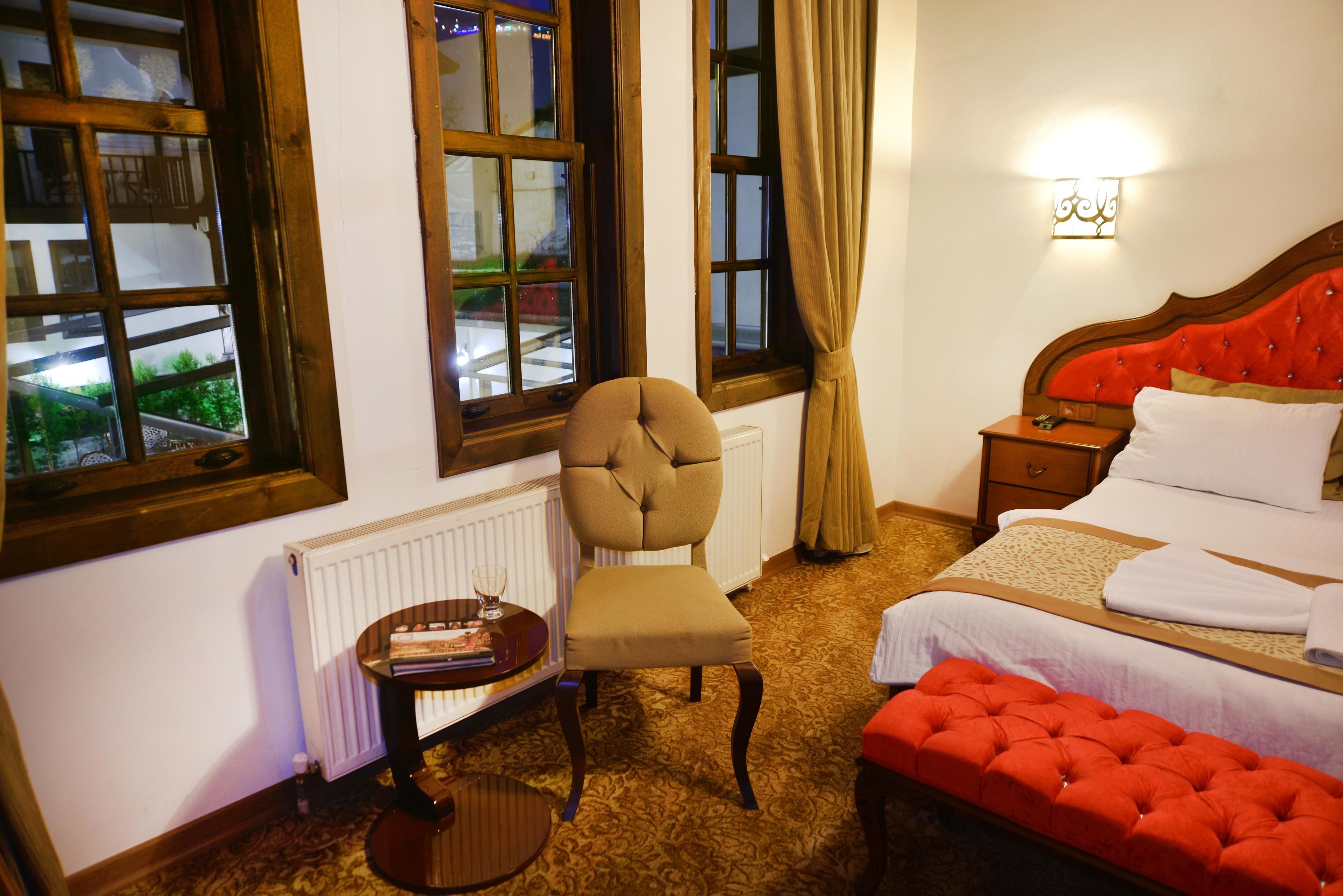A hotel room with a bed, a chair, a small table, and a window with curtains.