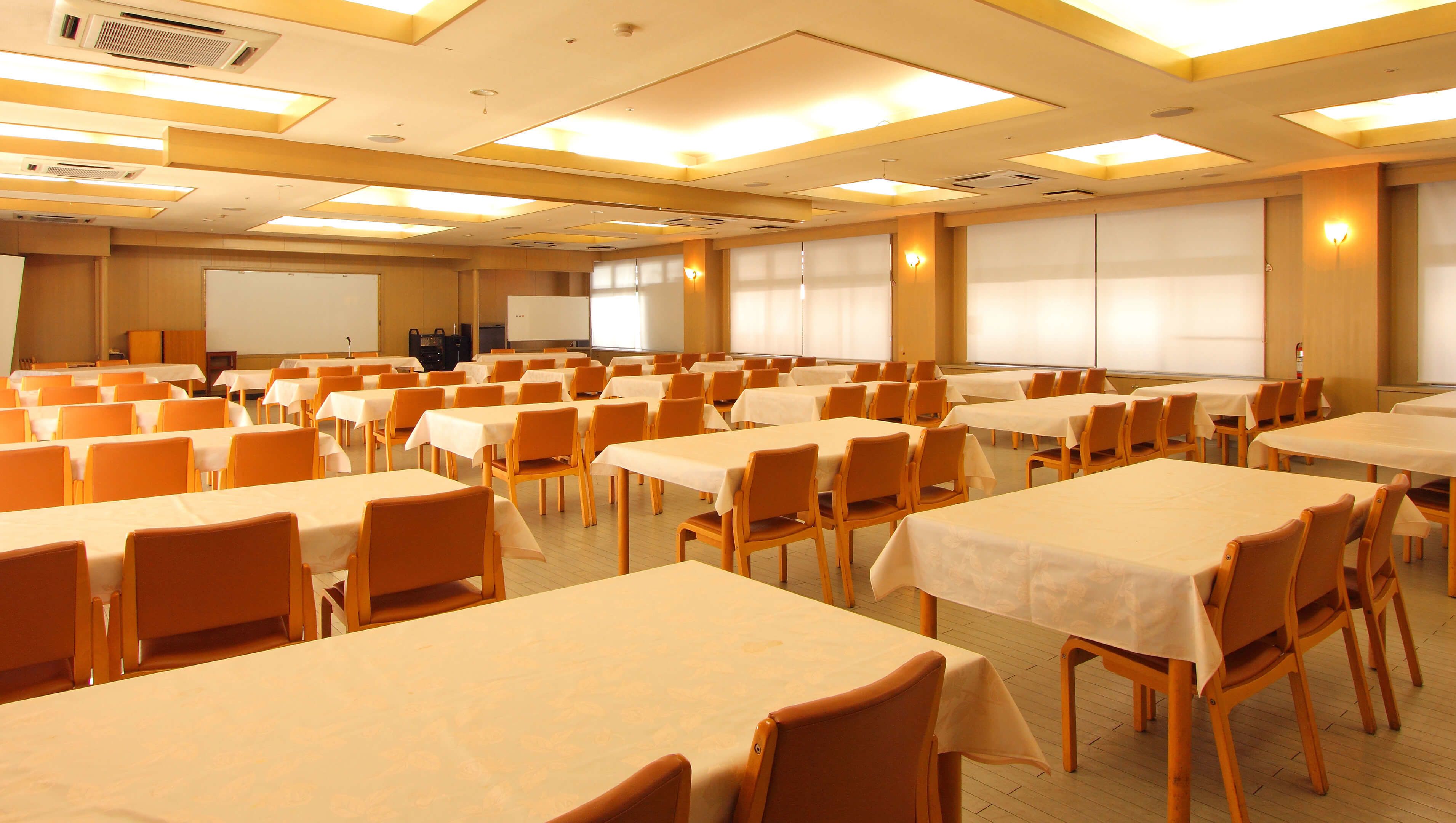 A conference room with multiple tables and chairs, equipped with ceiling lights and a whiteboard.