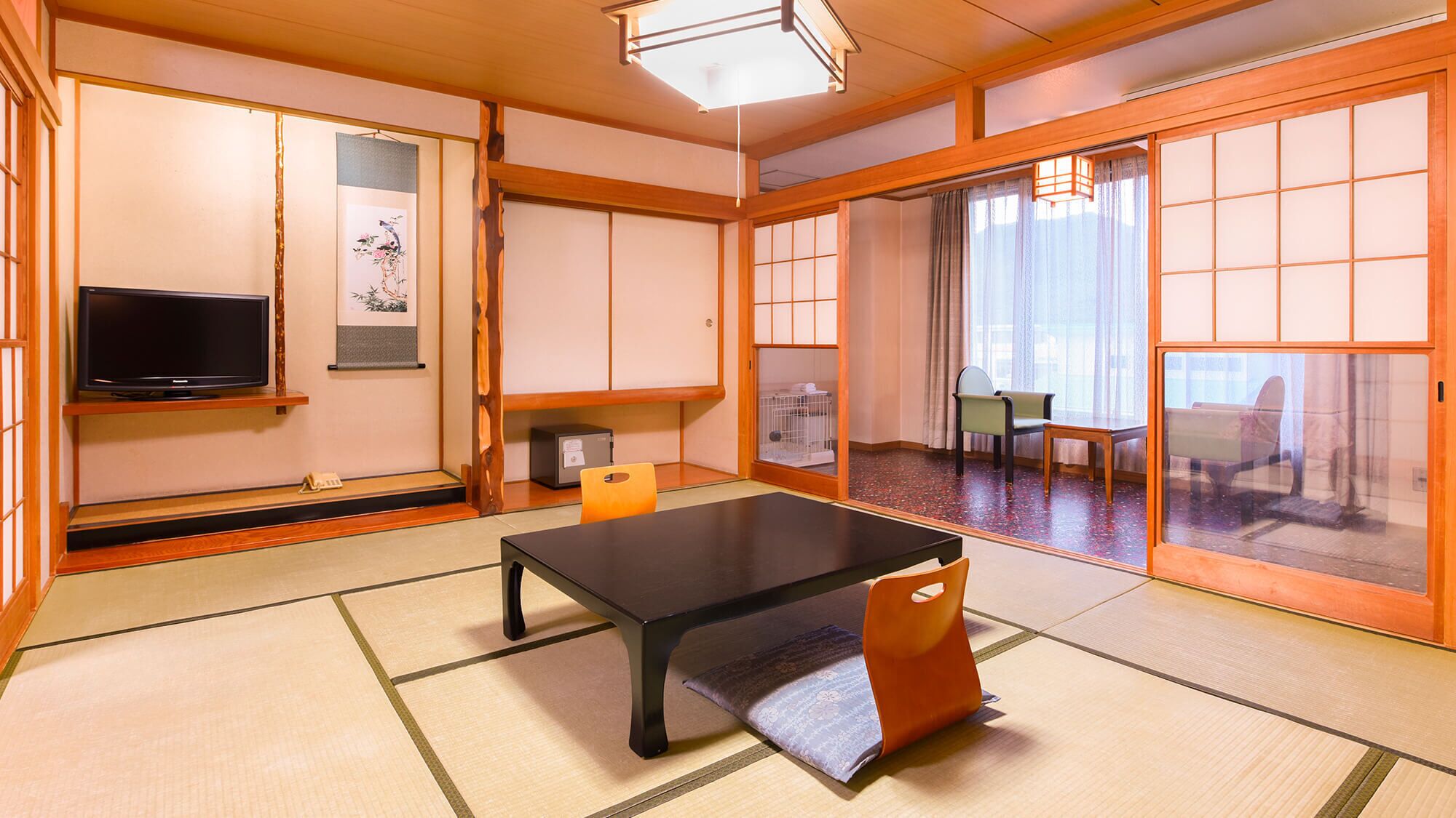 Ett traditionellt japanskt rum med tatamimattor på golvet, ett svart bord, en tv och skjutdörrar.