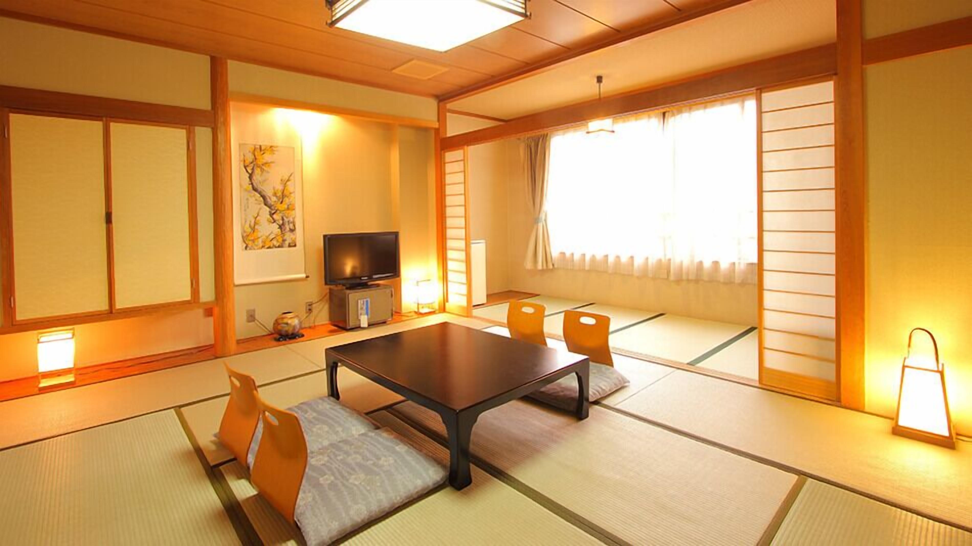 Ett traditionellt japanskt rum med tatamimattor på golvet, ett lågt bord, kuddar, en tv och skjutdörrar.