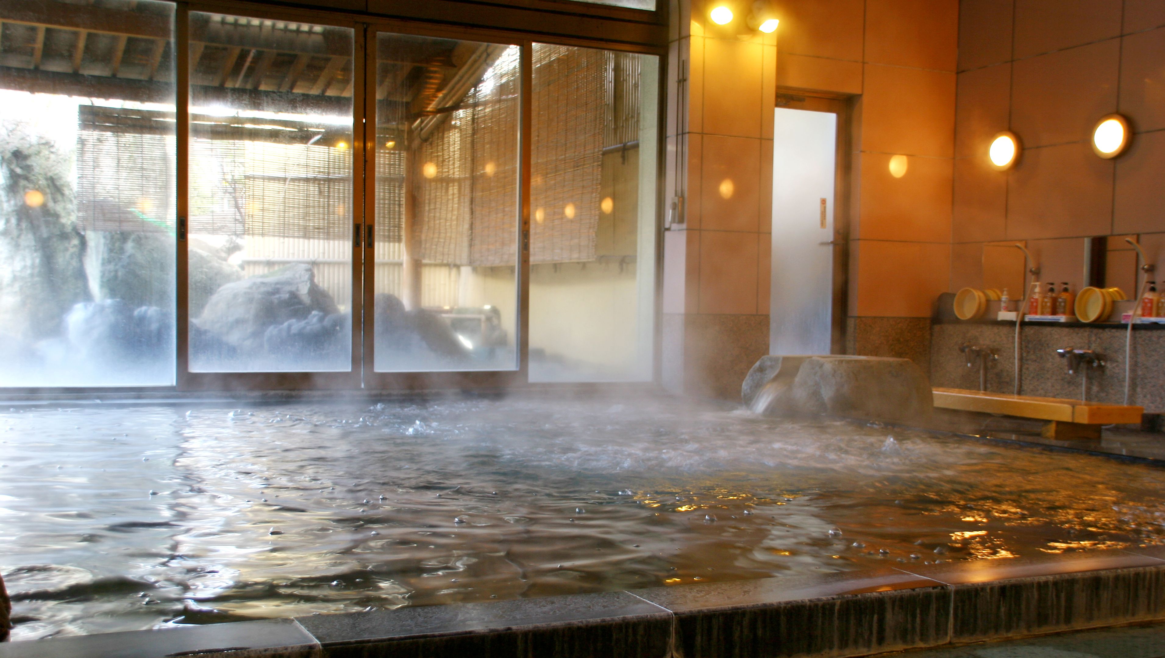 A hot spring bath with steam rising, a tiled floor, and a wooden bench.