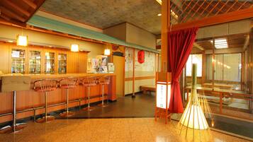 A traditional Japanese-style bar with wooden counters and stools, a tiled floor, and a red curtain.