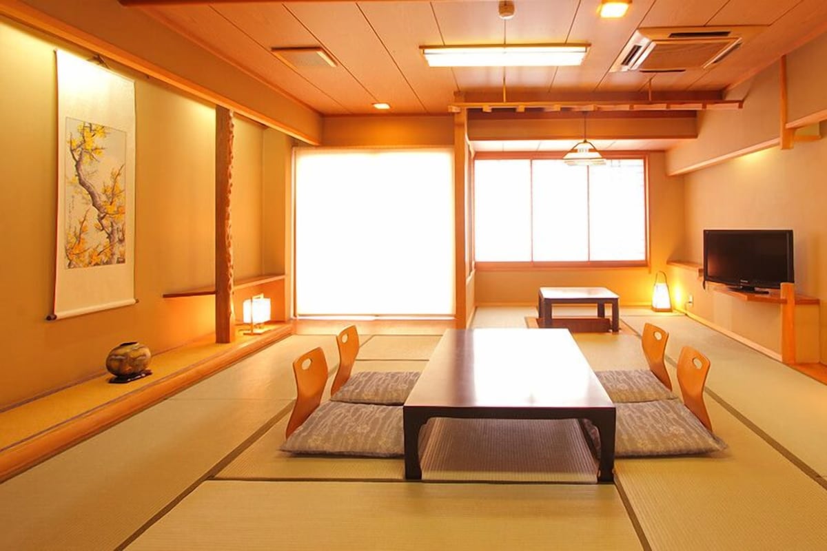 Una habitación de estilo japonés tradicional con suelo de tatami, una mesa baja y un televisor en la pared.