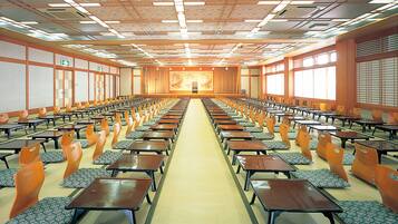 Un salón de conferencias con filas de mesas y sillas, suelo alfombrado y un techo al estilo japonés con vigas de madera y farolillos de papel.