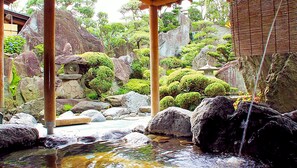 Un jardín japonés tradicional con un puente de piedra, una cascada pequeña y arbustos podados con cuidado.