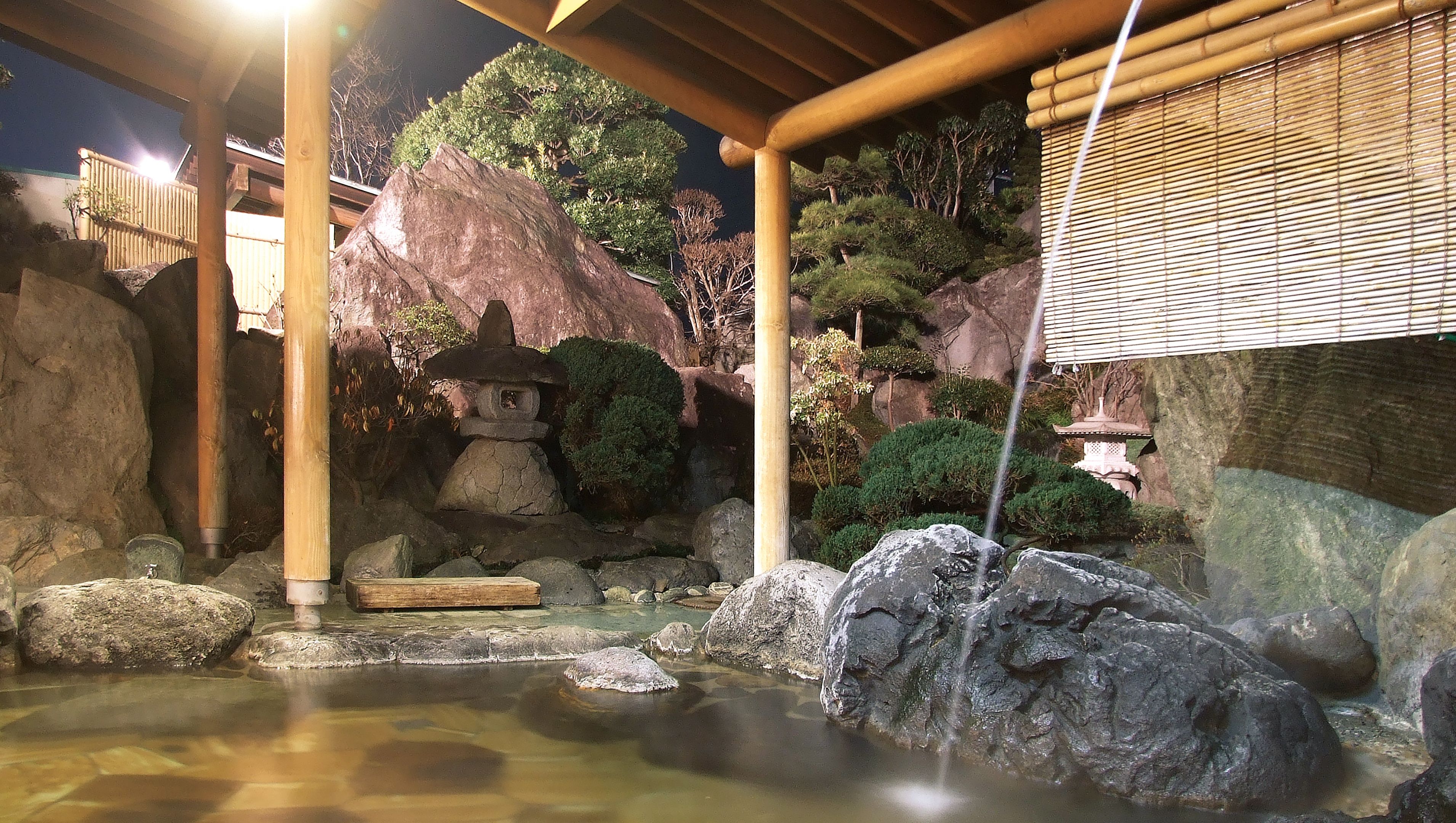 Un jardin japonais traditionnel agrémenté d’une lanterne en pierre, d’une petite cascade et d’un pavillon en bois.