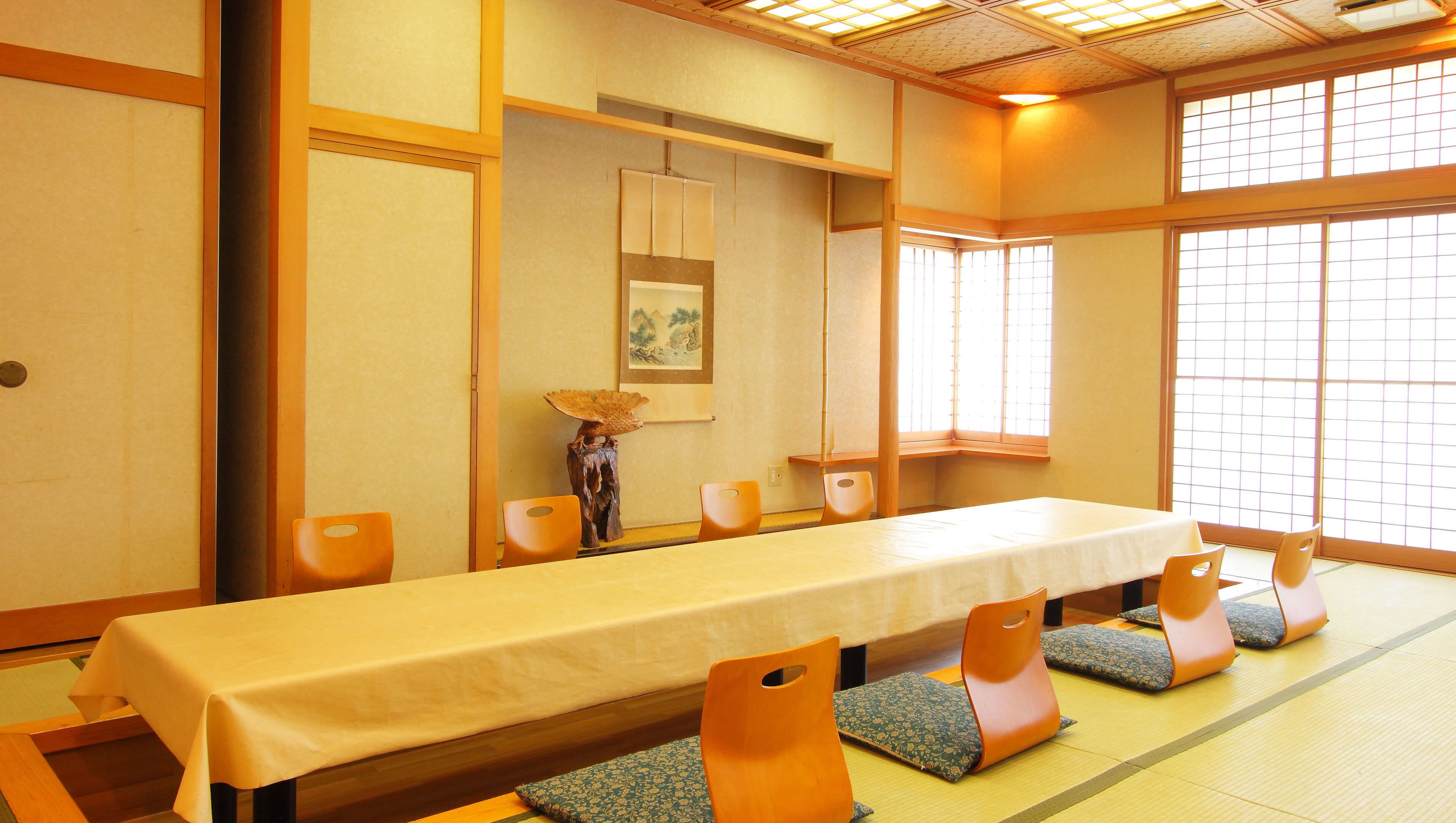 Ein traditionell gestalteter japanischer Raum mit Tatami-Böden, einem niedrigen Tisch und Holzstühlen mit Kissen.