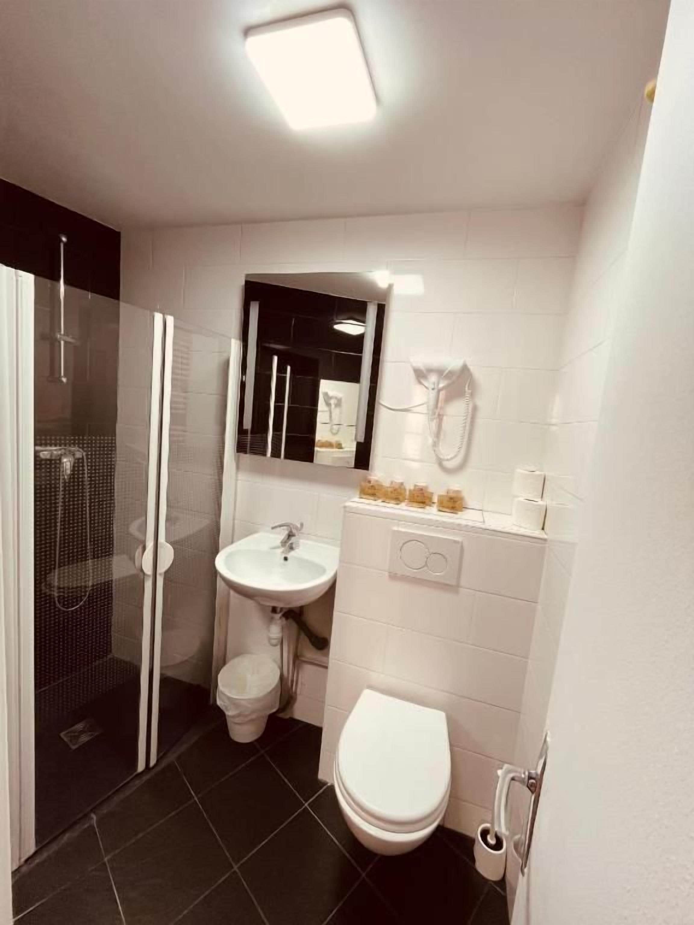 Ein kleines Badezimmer mit einer Duschkabine aus Glas, einem weißen Waschbecken, einer Toilette und einem Spiegel über dem Waschbecken.