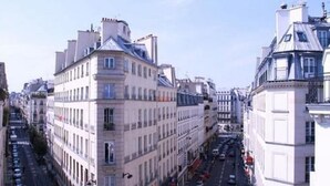 A street view of a city with historic buildings, narrow roads, and parked cars.