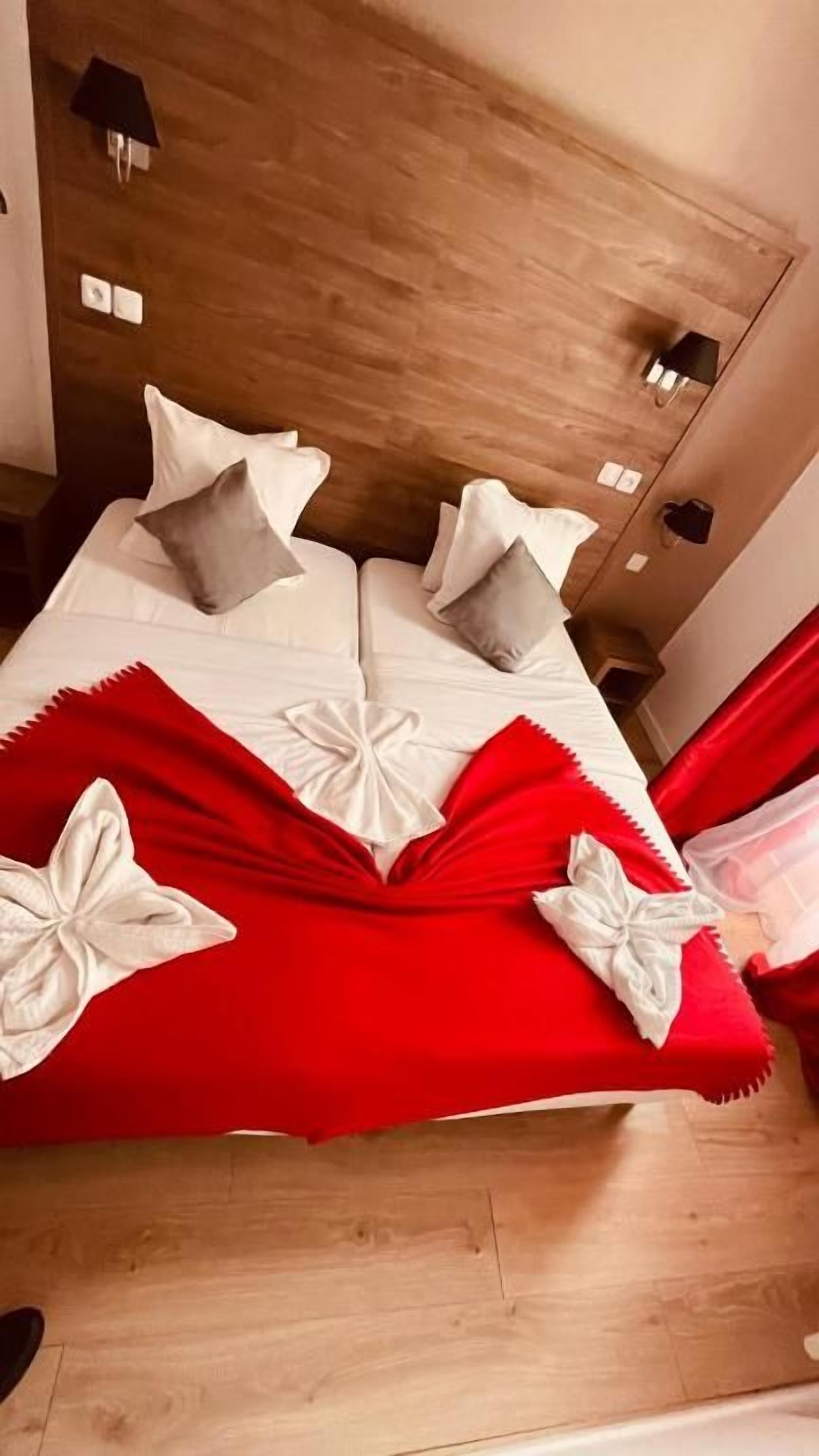 A bed with white bedding and red accents, a wooden headboard, and a mirror on the wall.