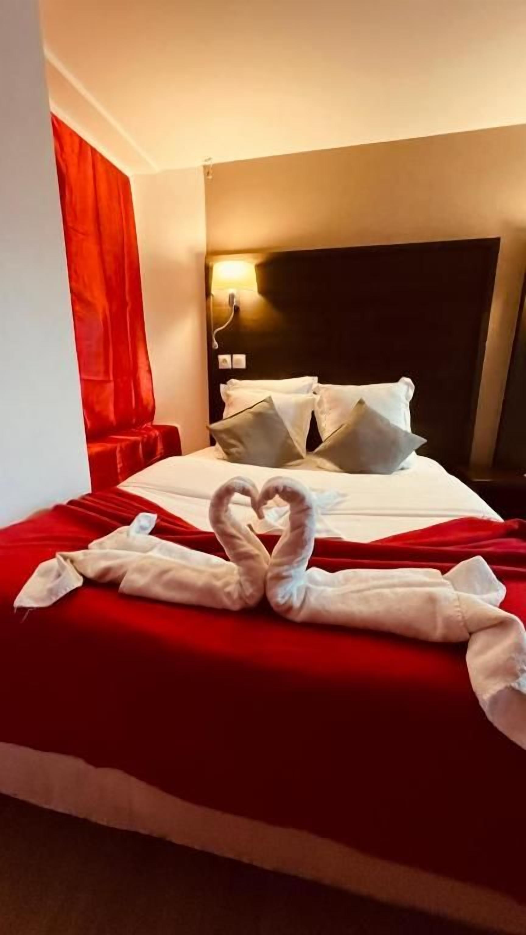 A hotel room with a bed, pillows, and a heart-shaped towel arrangement.