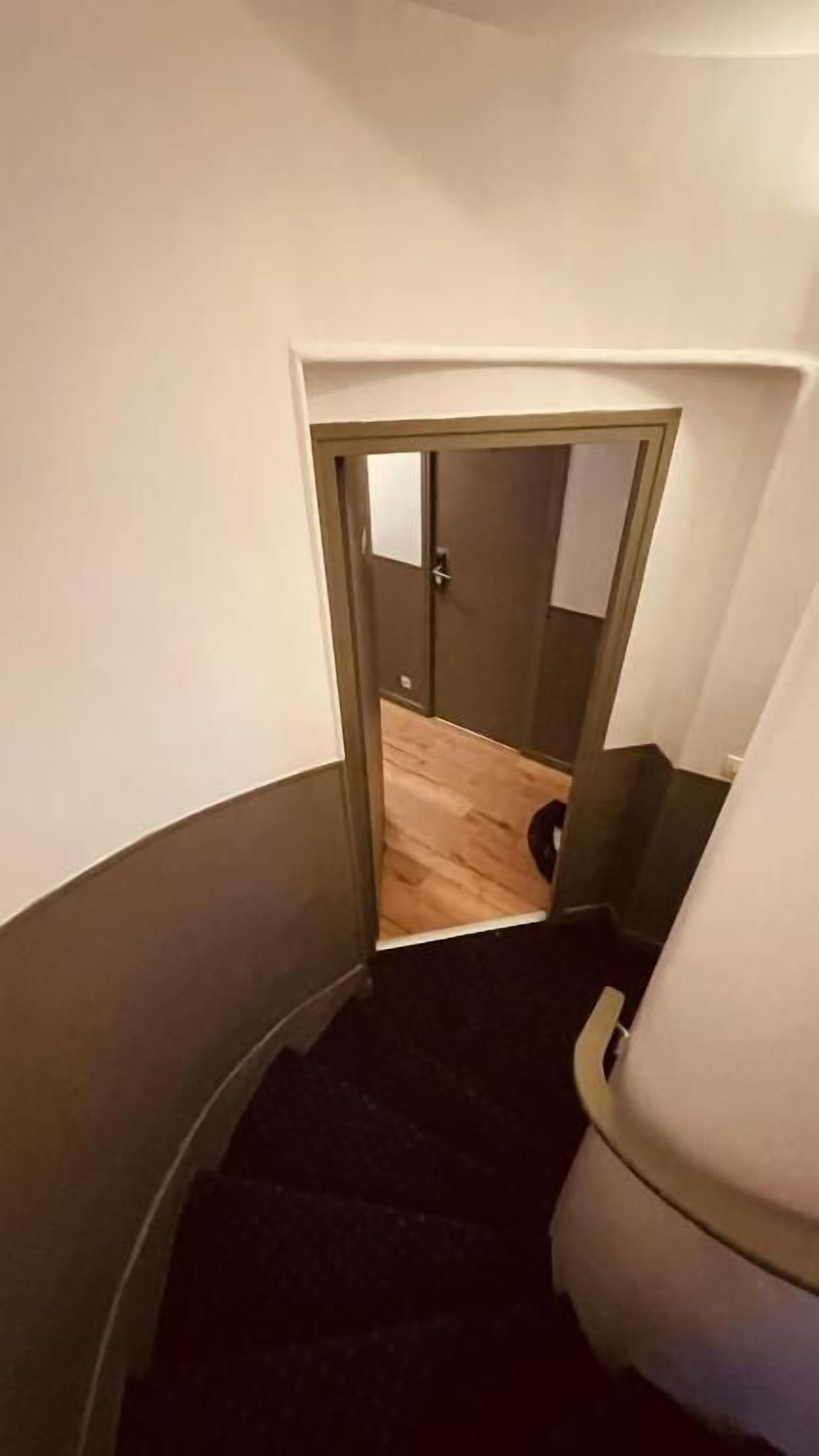 Un pasillo estrecho con una puerta que da a una habitación con piso de madera.