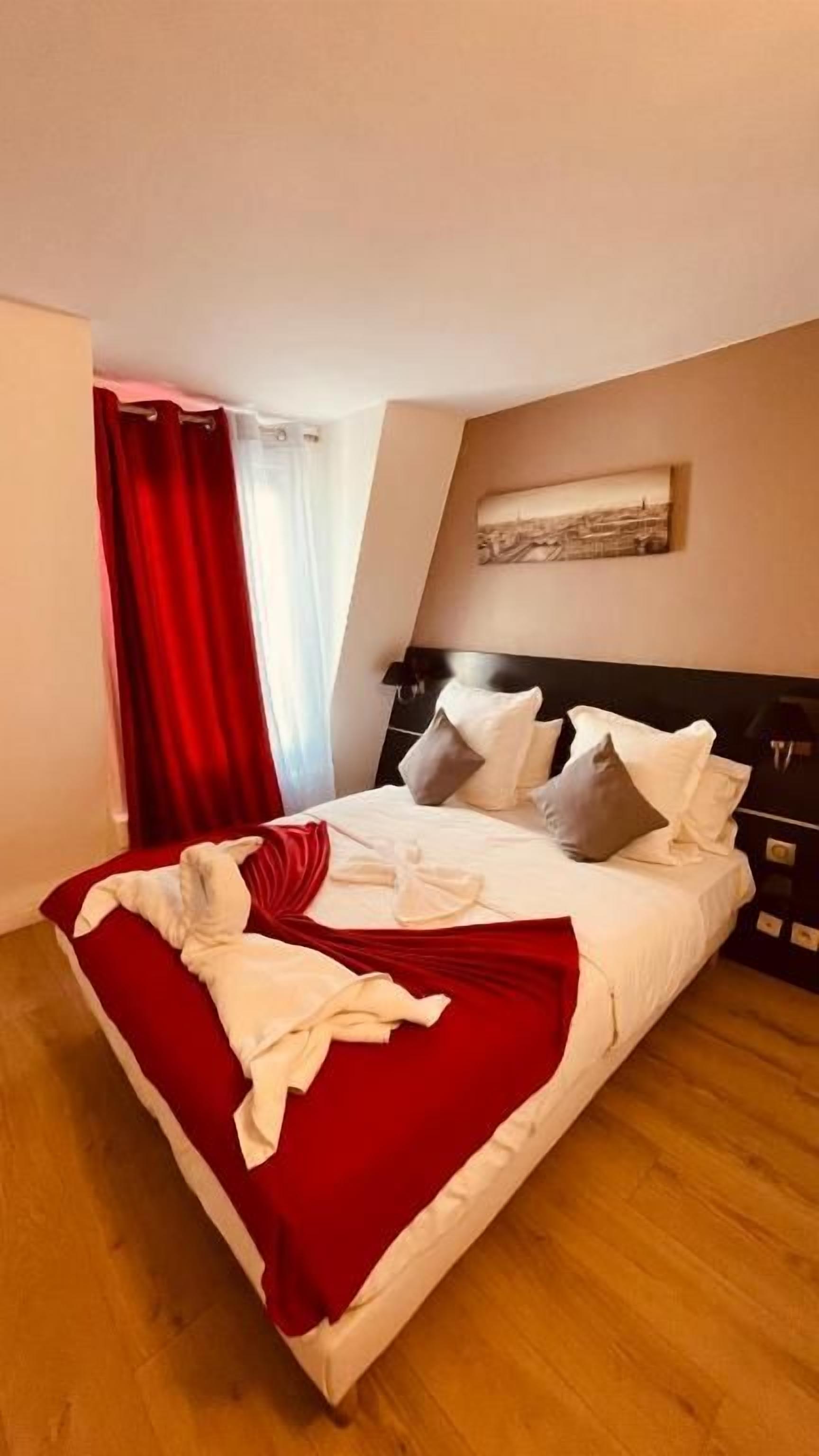 A neatly made bed with pillows and a red throw blanket, a wooden floor, and a painting on the wall.