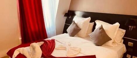 A neatly made bed with pillows and a red throw blanket, a wooden floor, and a painting on the wall.