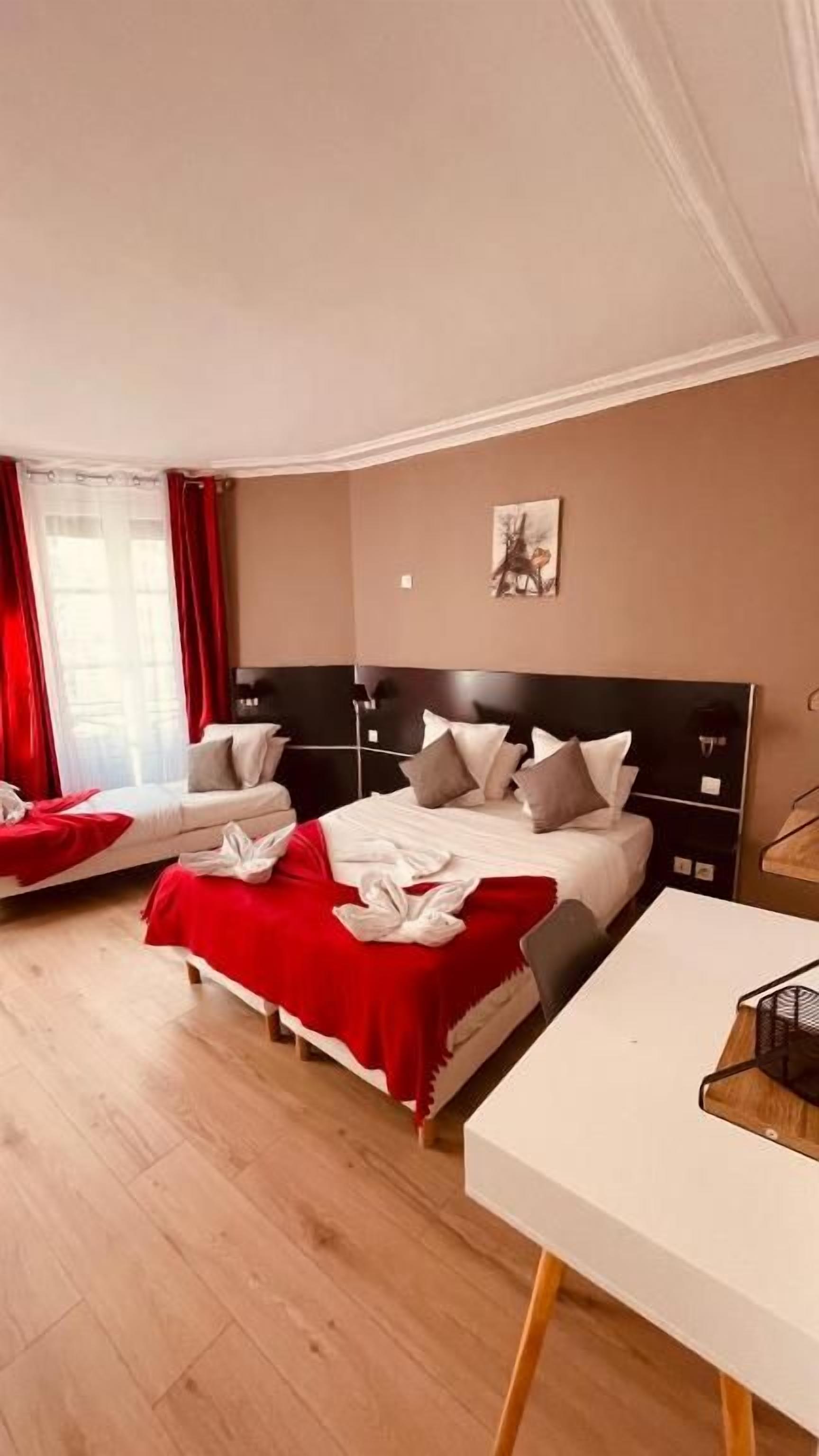 Habitación de hotel con dos camas, un escritorio y una ventana con cortinas rojas.