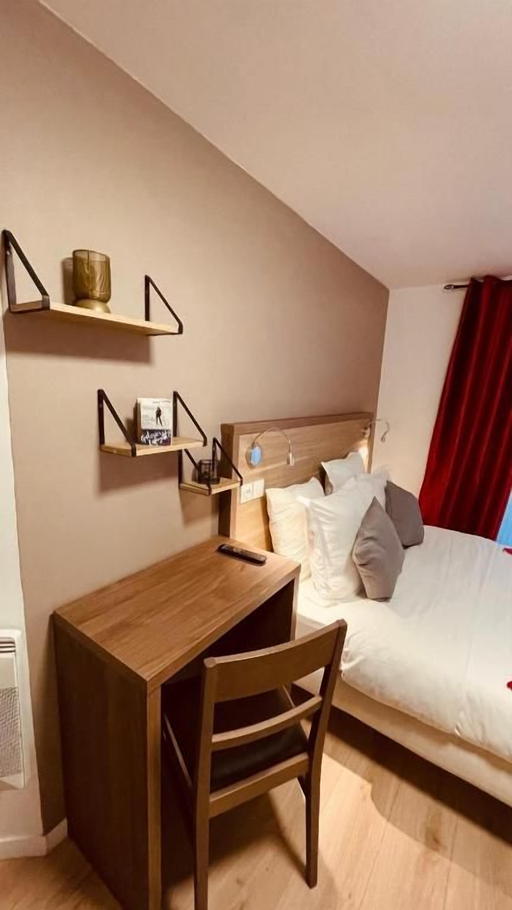 A bedroom with a bed, a wooden desk, and two wall-mounted shelves.