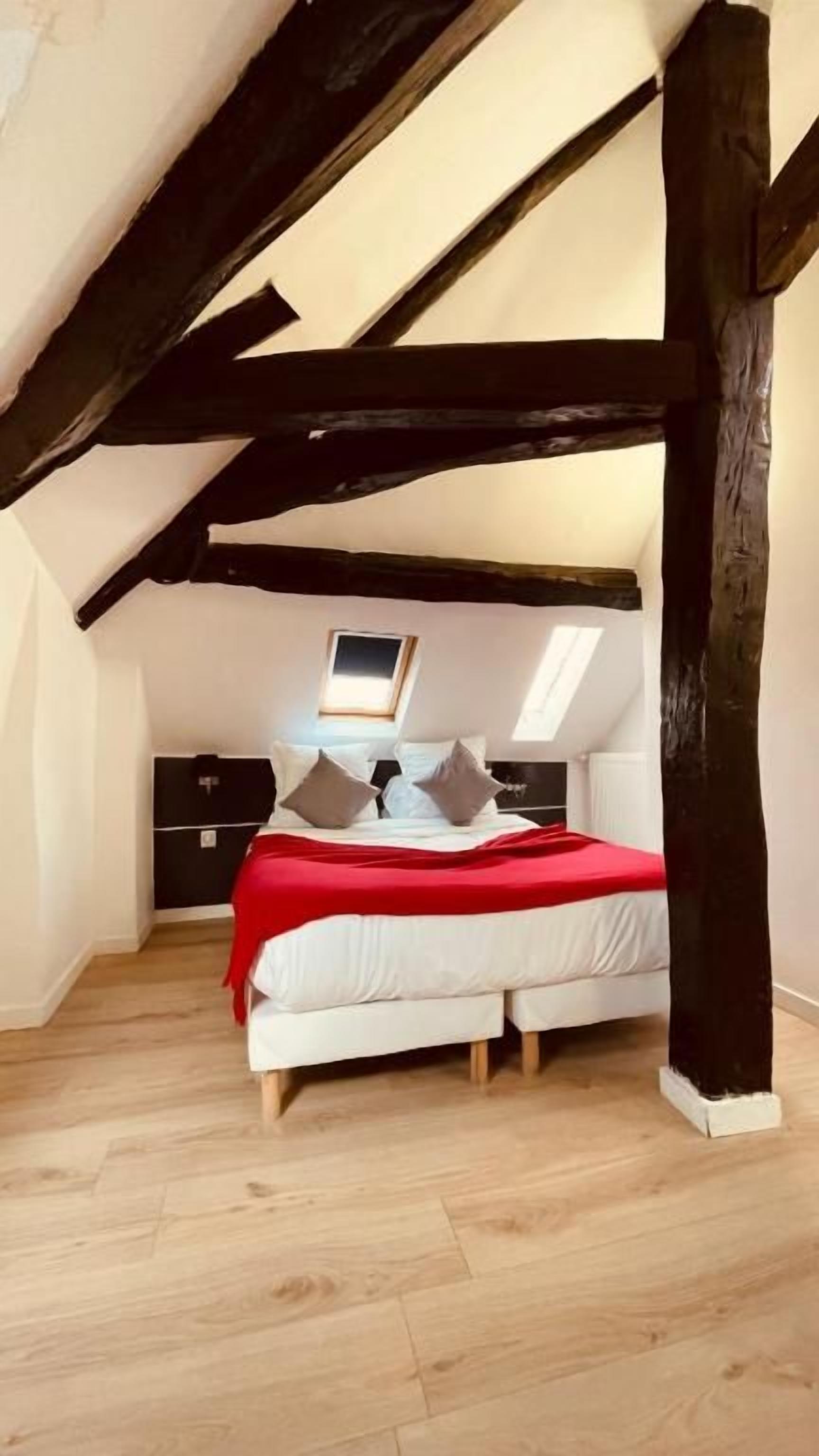 A bedroom with a sloped ceiling, a bed with a red blanket, and a small window.