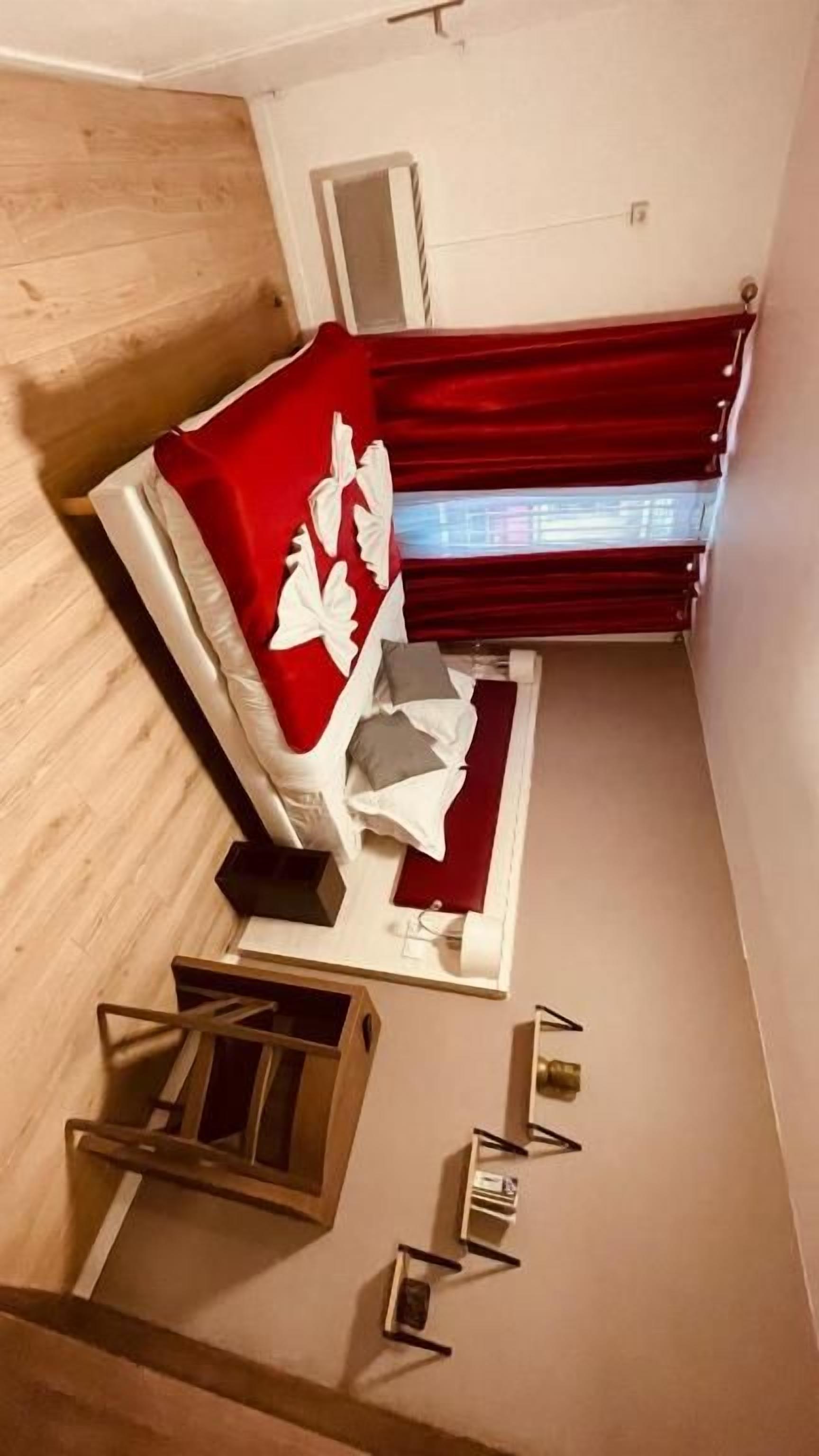 A room with a bed, a small table, a chair, a window with curtains, and a wooden floor.