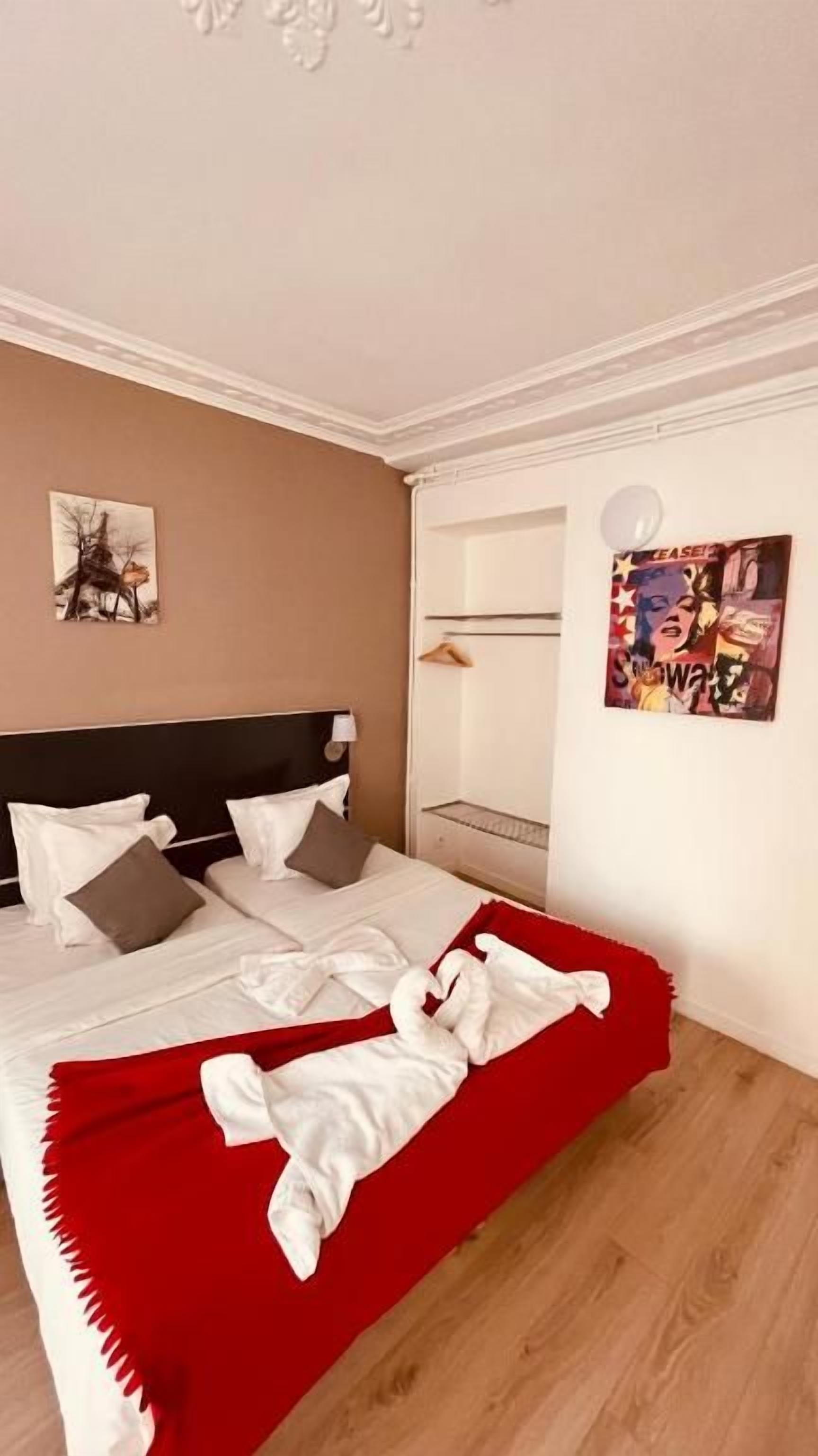 Quarto de hotel com cama, almofadas, manta vermelha e obras de arte nas paredes.