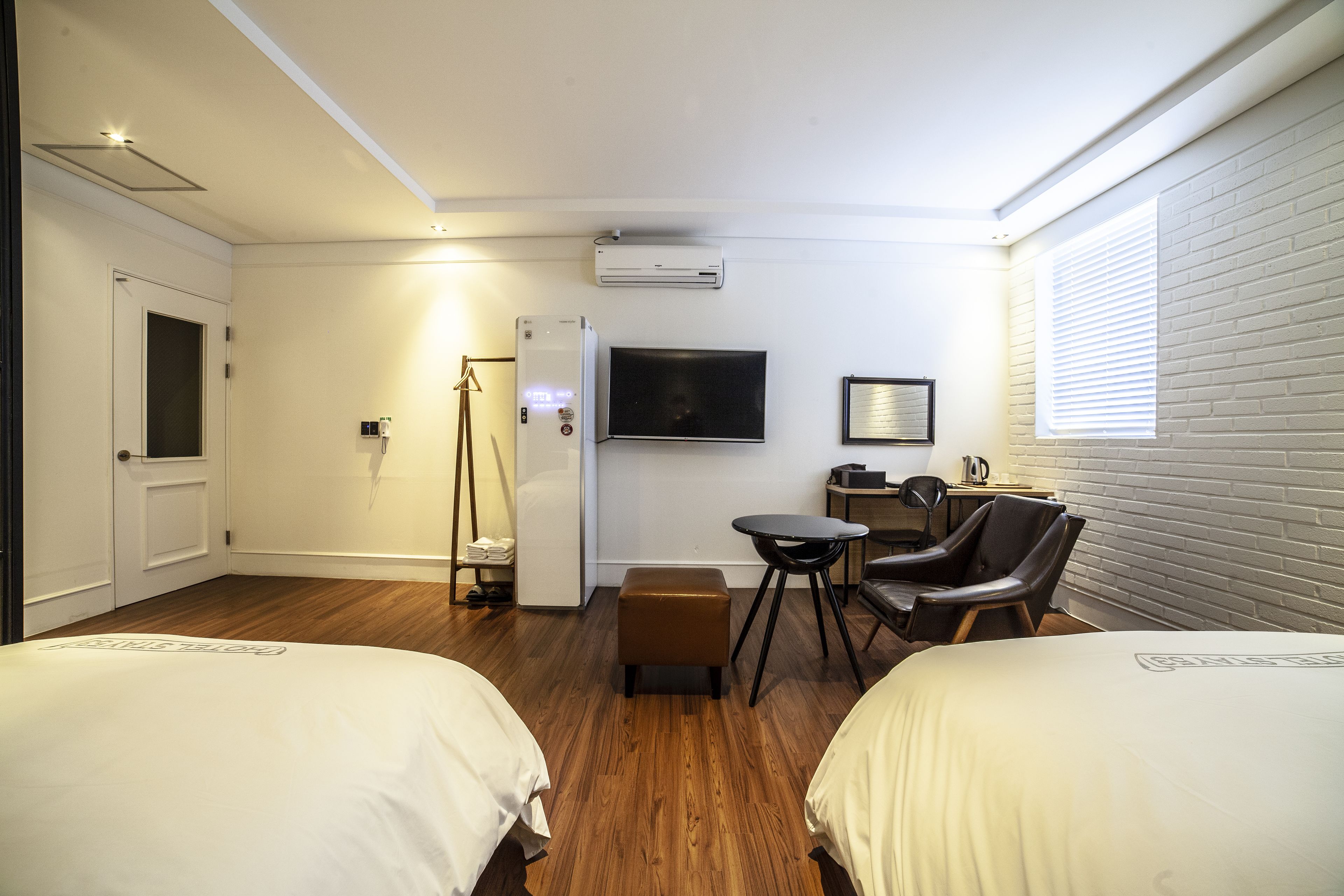 A hotel room with two beds, a desk, a chair, a TV, and a window with blinds.