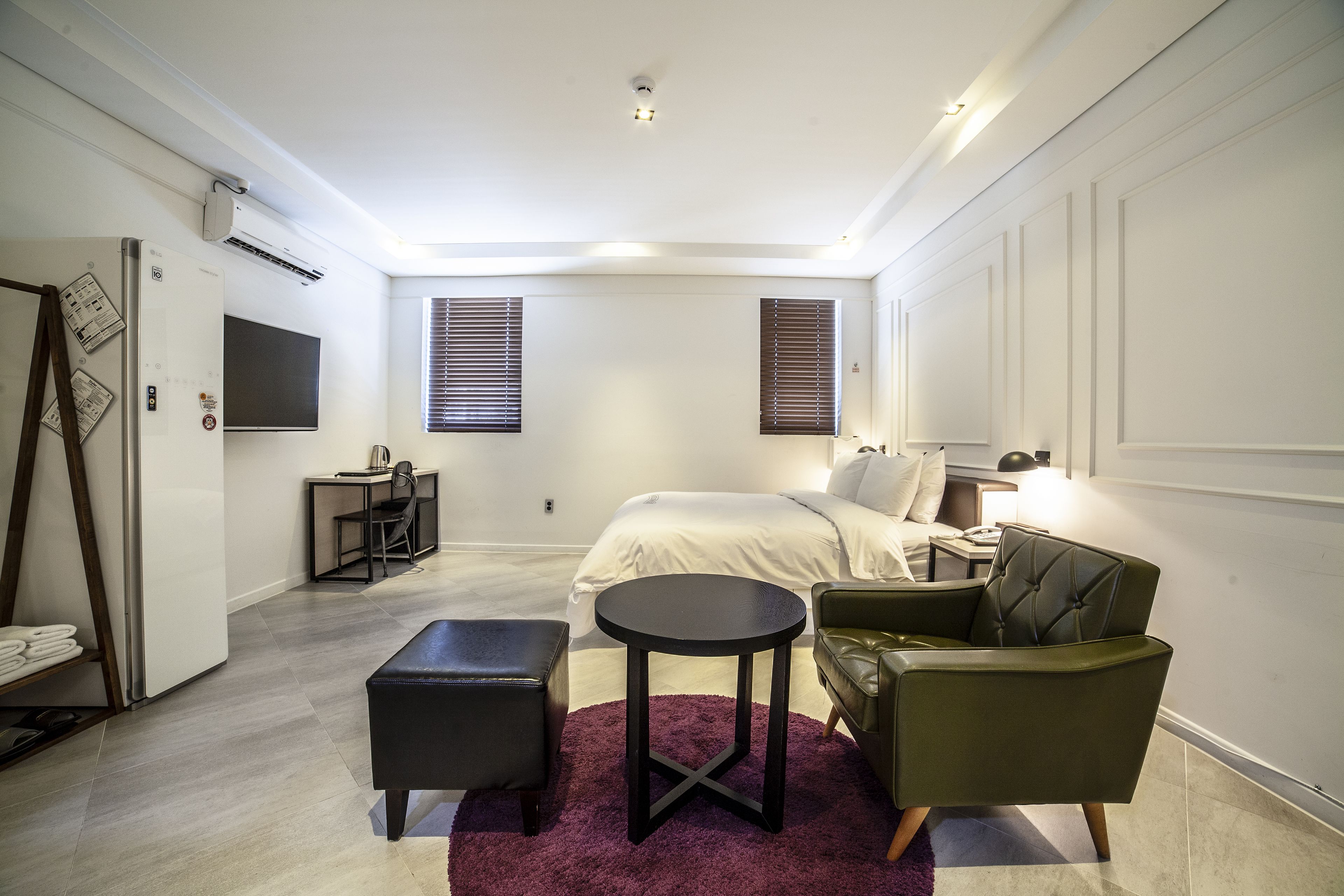 A modern bedroom with a bed, a desk, a chair, a small round table, and a purple rug.