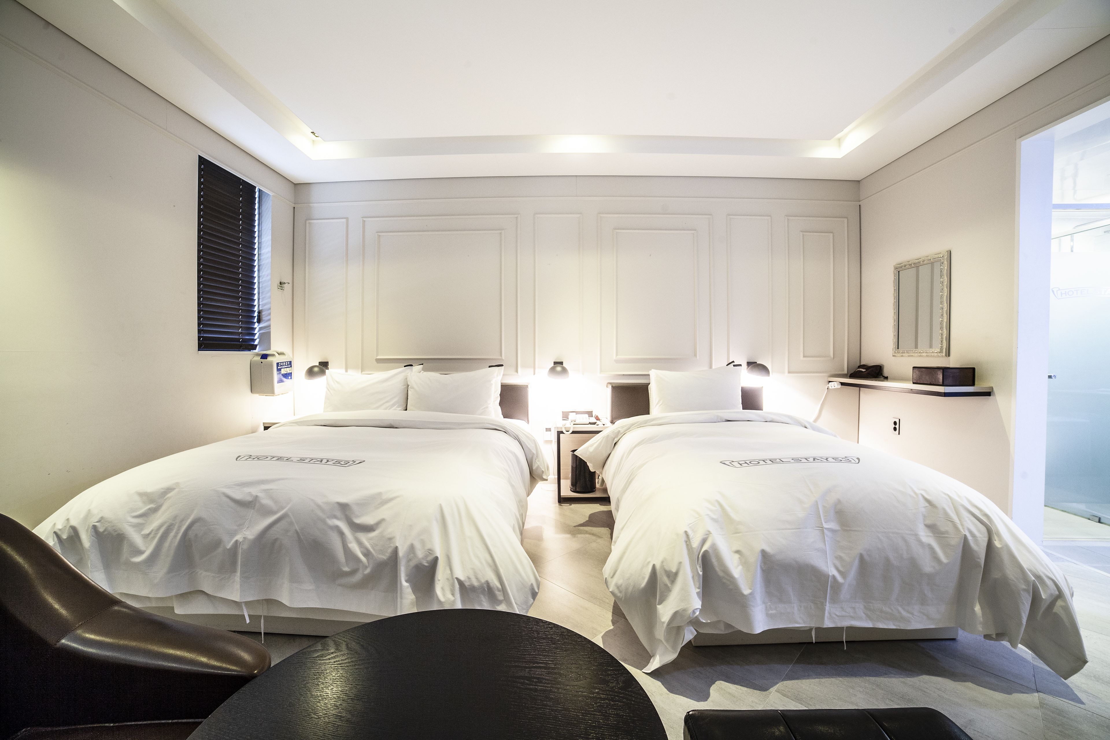 Habitación de hotel con dos camas, un escritorio, una silla y un ventanal grande.