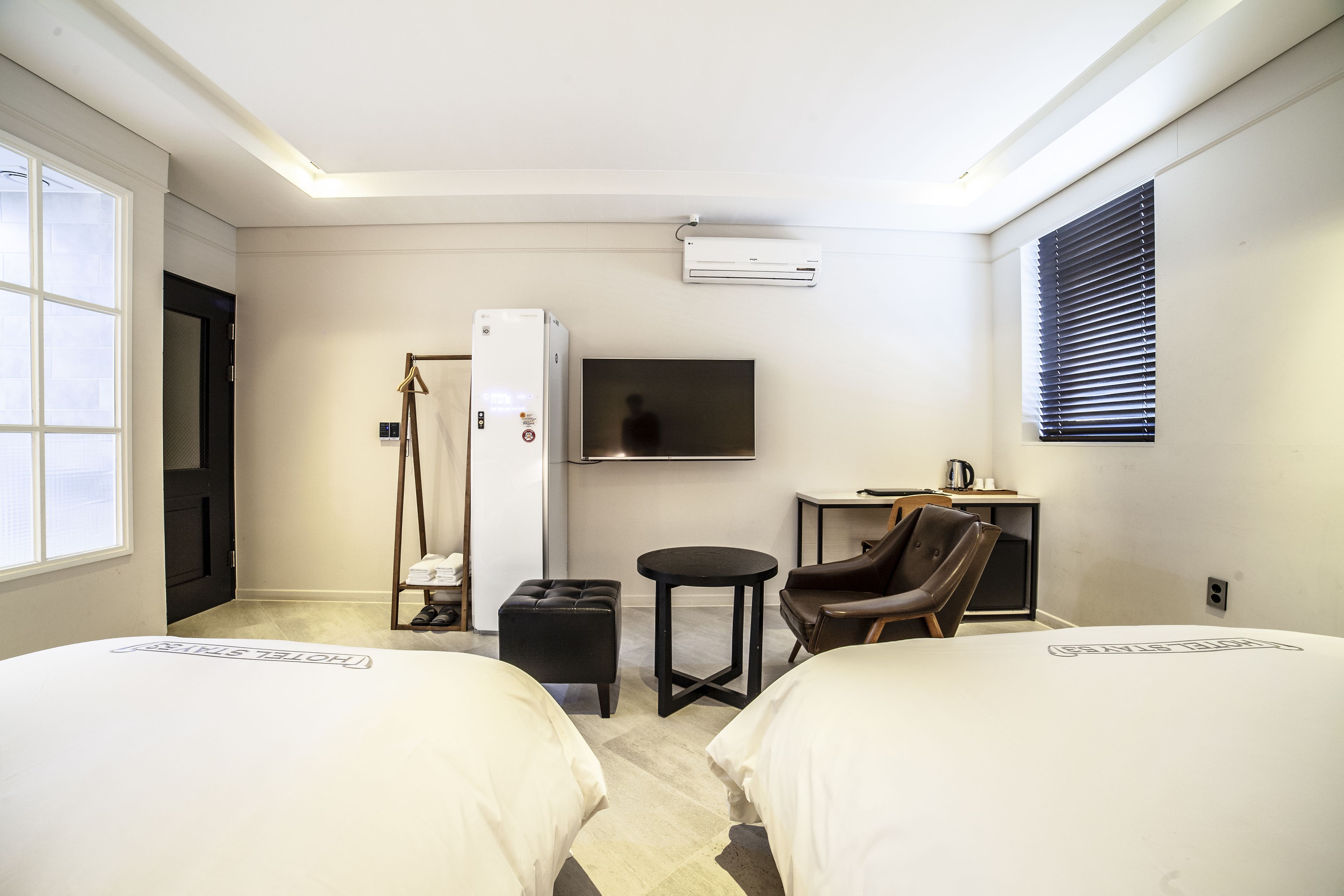 A hotel room with two beds, a TV, a small table, a chair, and a wardrobe.