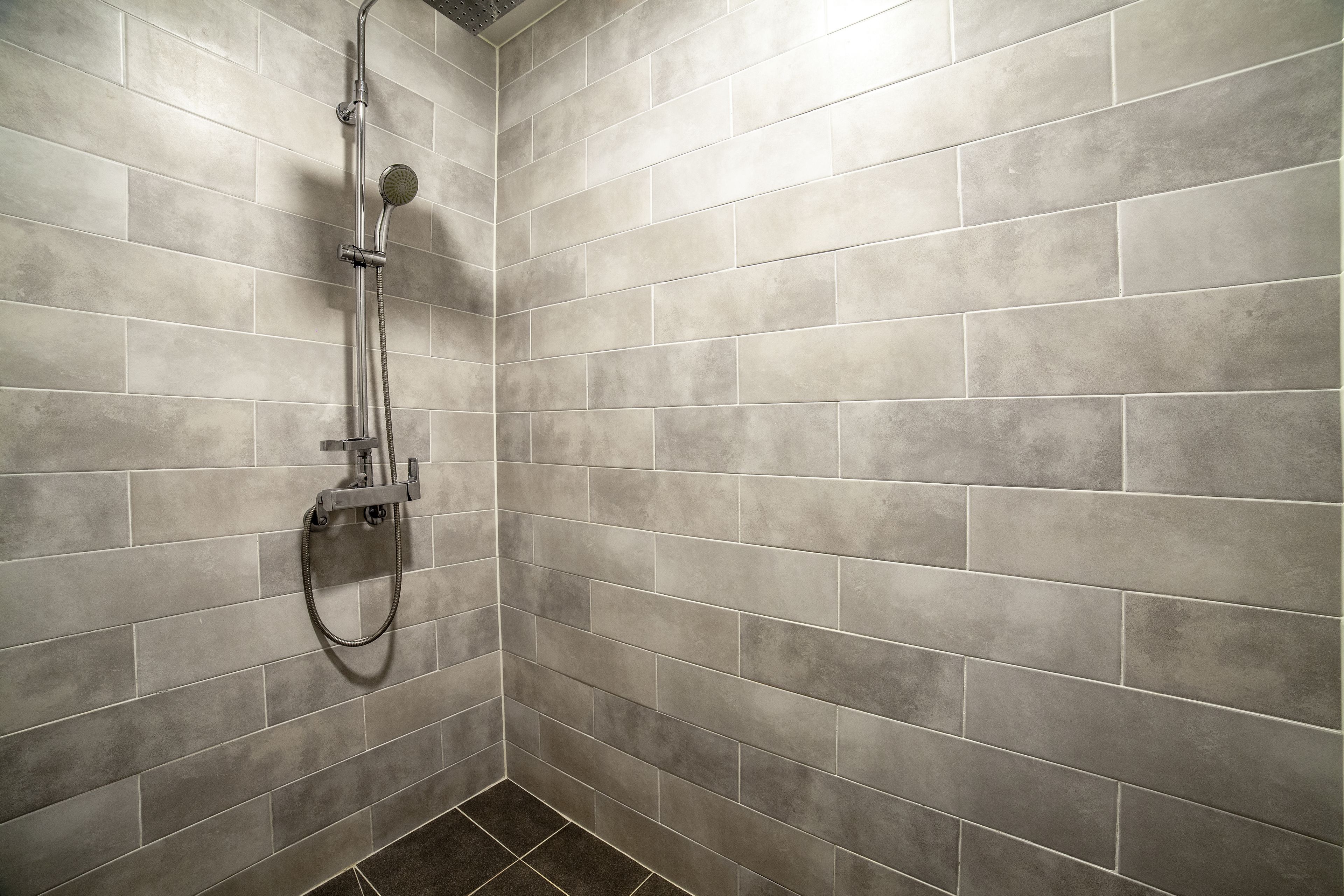 A shower area with a handheld showerhead and a wall-mounted faucet.