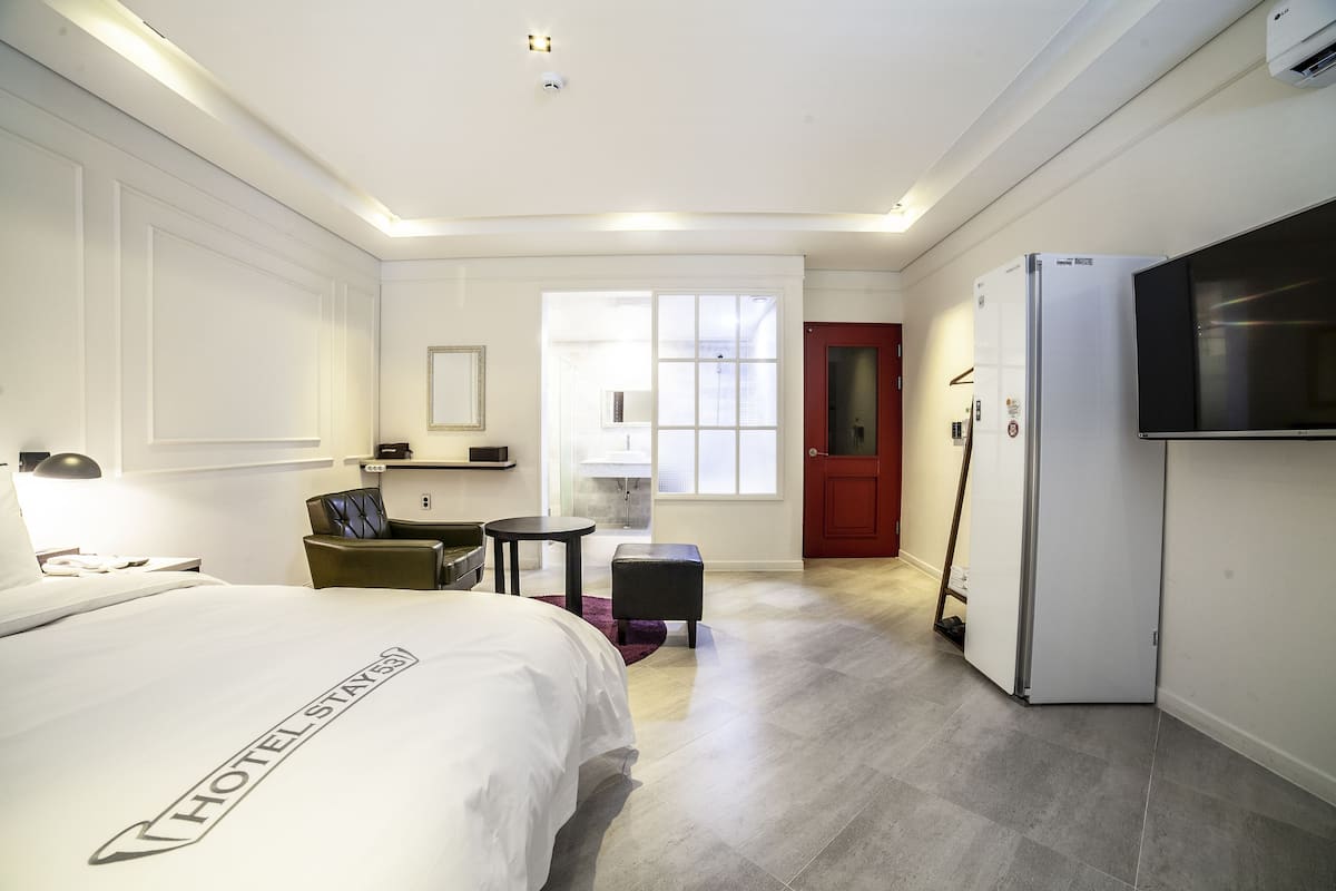 A hotel room with a bed, a desk, a chair, a television, and a refrigerator.