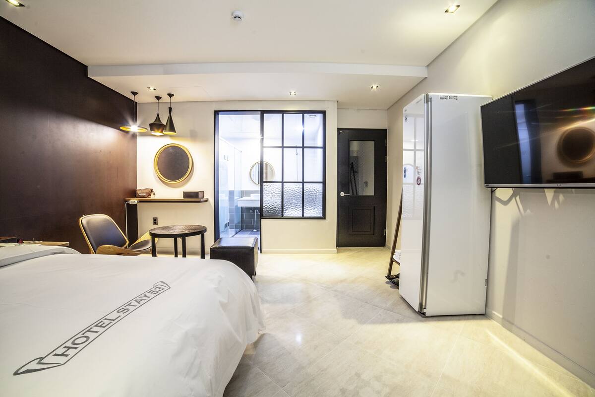 A hotel room with a bed, a desk, a chair, a TV, and a refrigerator.