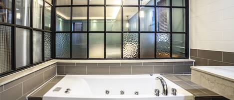 Un baño moderno con una bañera grande, una ventana con vidrio decorativo y piso de baldosas.