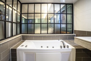 Un baño moderno con una bañera grande, una ventana con vidrio decorativo y piso de baldosas.
