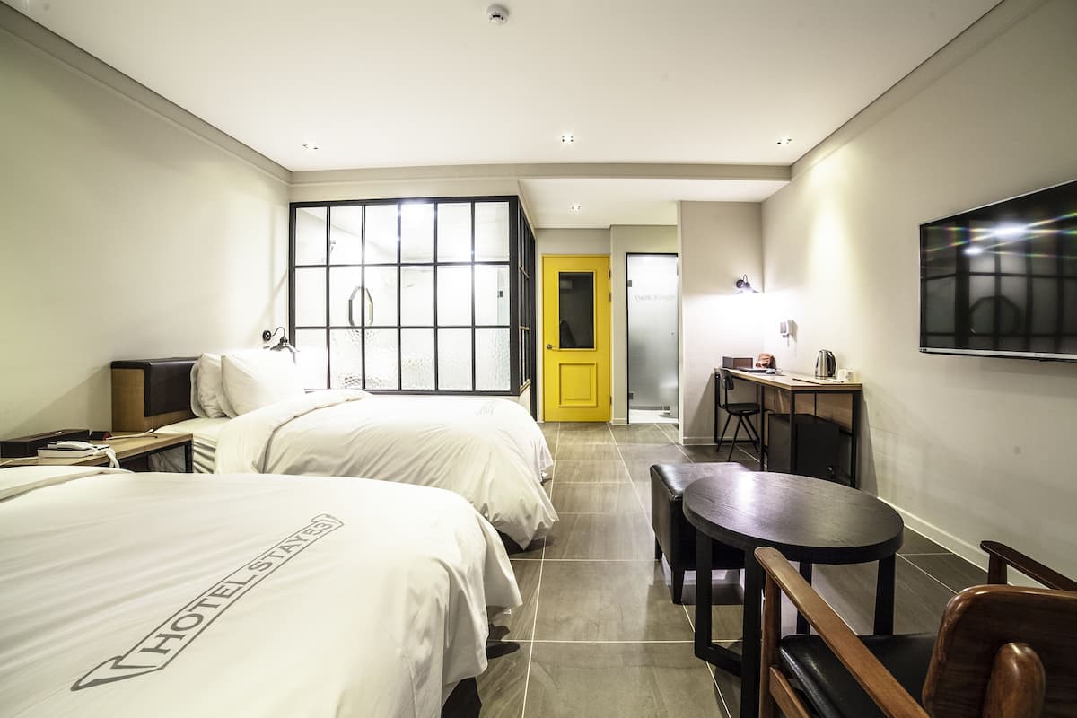 A hotel room with two beds, a desk, a chair, a TV, and a window with a view.