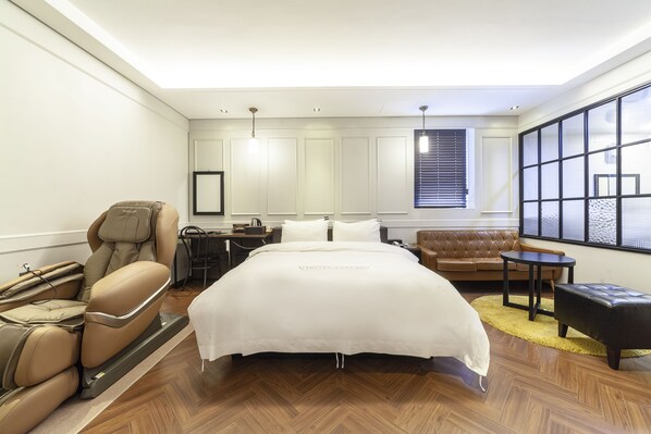 Una habitación de hotel con una cama grande, sillón de masaje, sofá y una mesita.