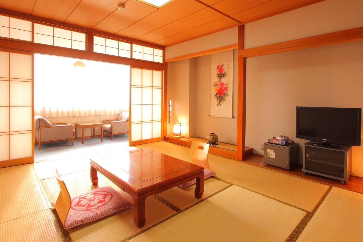 A traditional Japanese room with tatami flooring, a low wooden table, a sofa, a television, and a cabinet.