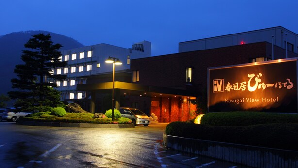 Ein Hotel Eingang mit einem Schild, das 'Kasugai View Hotel' zeigt, und ein Parkplatz mit Autos.