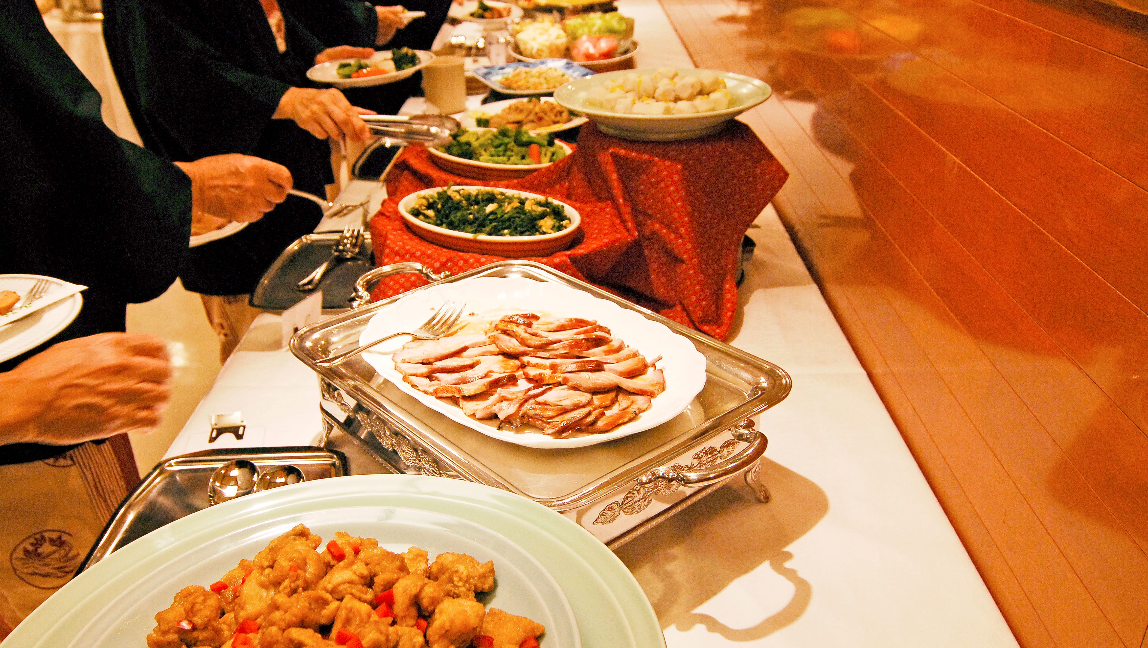 Una mesa de buffet con diversos platos, incluyendo una bandeja grande de carne en rodajas y un tazón de verduras mixtas.