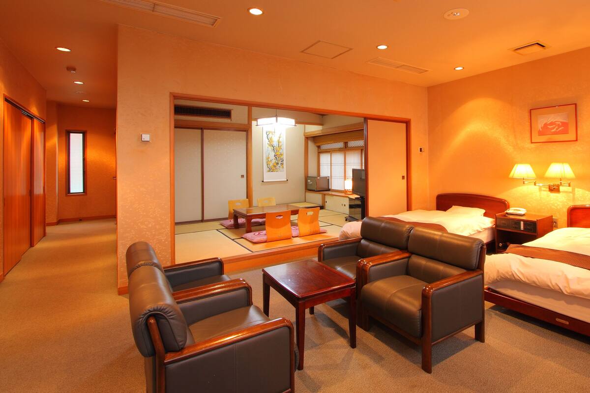 A hotel room with a bed, two chairs, a small table, a desk, a TV, and a lamp.
